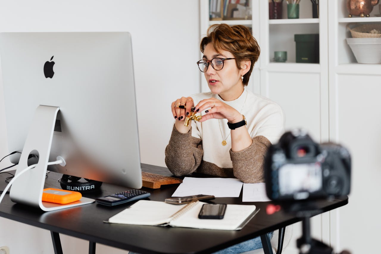 about-02 A professional woman engaged in a virtual meeting setup at her home desk, using a computer and camera.