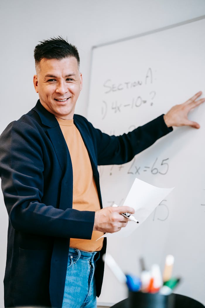 ours-journey Friendly teacher explains equations on a whiteboard in a classroom setting.